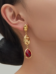 Detail of gold-plated teardrop earrings with red crystal stones worn by a model