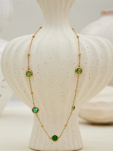 Detail of 18k gold plated long necklace with faceted green glass stones on a ceramic vase