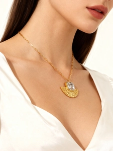 Gros plan d'un collier doré avec pendentif en éventail texturé et pierre transparente
