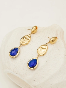 Macro shot of 18k gold teardrop earrings with faceted blue glass stone in bezel setting