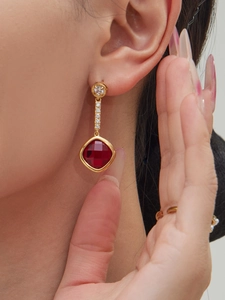 Close-up of gold earrings with square red gemstone and white zircon accents