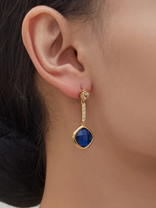 Close-up of gold drop earrings with zircon accents and a square blue gemstone