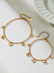 Close-up of gold heart charm bracelets with zircons and S.Steel tag on white stone