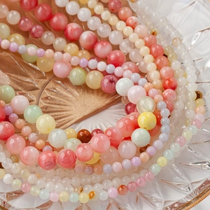 Natural round green jade and multi-color gemstone beads displayed on a glass tray