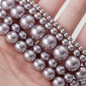 Perlas de vidrio moradas en varios tamaños para joyería DIY mostradas sobre una palma