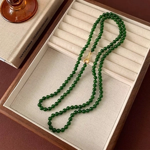 Detailed close-up of dark green 8mm beads with gold metal S-clasp on wooden tray