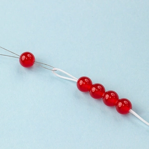 Proceso de joyería DIY con cuentas rojas y alambre de acero sobre fondo azul