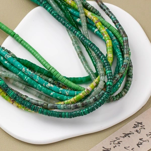 Dettaglio macro di fili di perle heishi verdi in un piatto di ceramica bianca a cuore