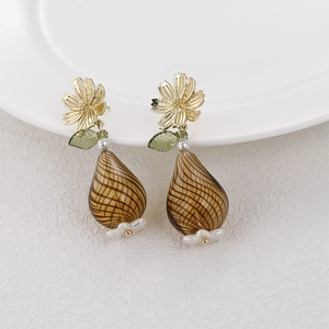 Floral gold earrings with green leaves and amber striped glass fruit pendants on white tray