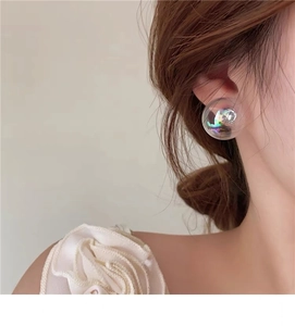 Close-up of a 2cm iridescent glass bubble earring worn with a white floral organza top