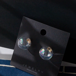 Close-up of iridescent glass bubble earrings with colorful glitter on black display card