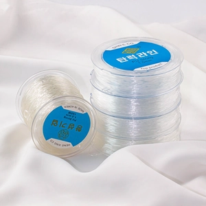 Macro shot of 1.0mm clear elastic PU string rolls for DIY jewelry on white silk