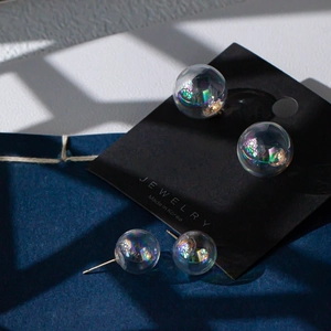 Iridescent glass bubble earrings with gold studs displayed on a premium jewelry card