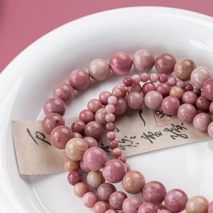 Macro view of natural pink stone beads in various sizes on a white ceramic dish