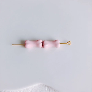 Vue détaillée de perles roses en forme d'os sur tige dorée pour bijoux DIY
