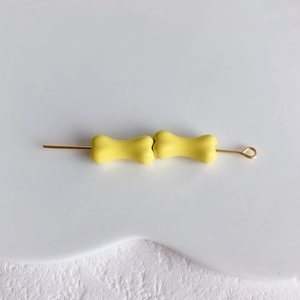Vue macro de deux perles en forme d'os jaune clair sur des épingles à bijoux dorées