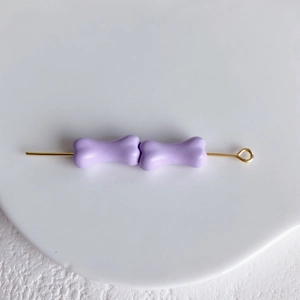 Détail de deux perles en forme d'os violet clair sur une tige dorée pour bijoux DIY
