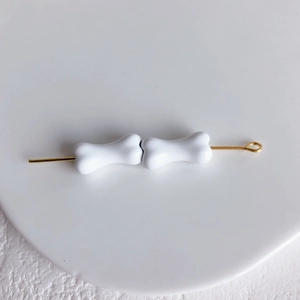 Détail de perles blanches en forme d'os sur une épingle dorée pour bijoux DIY