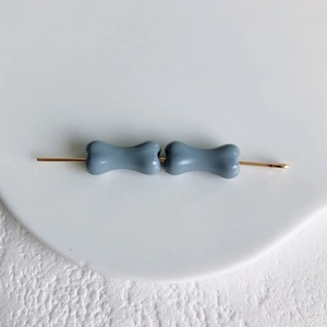 Détail d'une pince à cheveux os avec breloques gris mat sur une base en métal doré