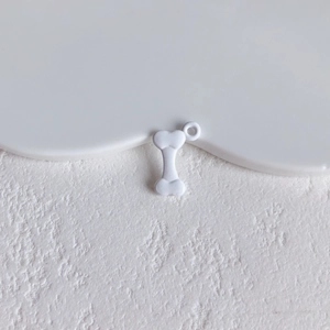 Close-up of white bone-shaped matte alloy charm with hanging ring for DIY jewelry making