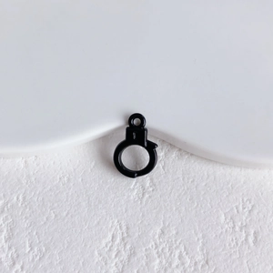 Macro shot of black matte handcuff-shaped DIY jewelry pendant on white textured surface