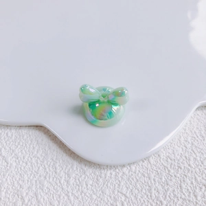 Close-up of mint green iridescent bow charm with laser finish on a white display tray