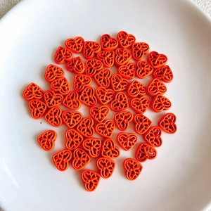 Close-up of bright orange hollow heart beads with floral cutouts for DIY jewelry making