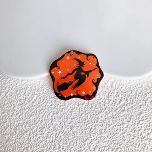 Dettaglio di un ciondolo di Halloween in acrilico con silhouette di strega nera su arancio