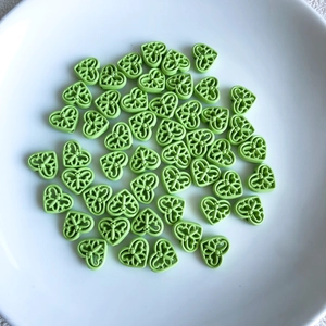 Close-up of light green heart-shaped hollow beads with butterfly patterns for DIY jewelry