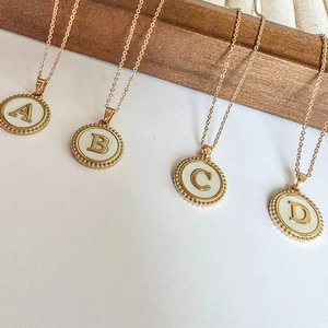 Gold stainless steel letter pendants with freshwater shell inlay on wooden display