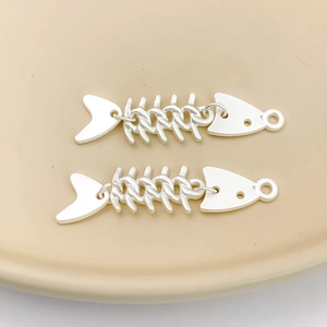 Dettaglio macro di due ciondoli a lisca di pesce in argento su piatto di ceramica