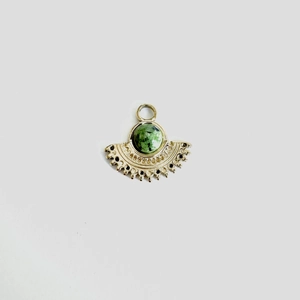 Detailed close-up of a fan-shaped gold pendant with a round green gemstone inlay