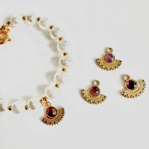 Detailed macro view of fan-shaped gold pendants with red stones and a pearl bracelet