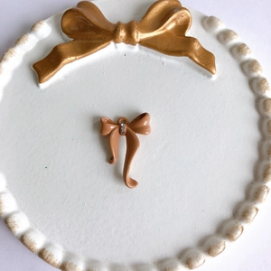 Detalle macro de colgante de lazo crema con tres diamantes pequeños para joyería DIY