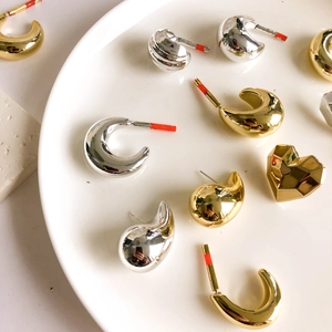 Minimalist gold and silver acrylic hoop earrings in heart and drop shapes on a tray
