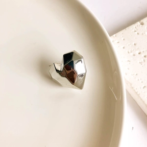 Close-up of faceted silver heart-shaped earring on ceramic plate with modern geometry