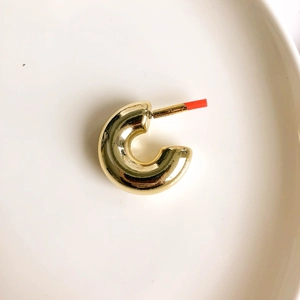 Close-up of chunky gold C-shaped hoop earrings on a white porcelain plate