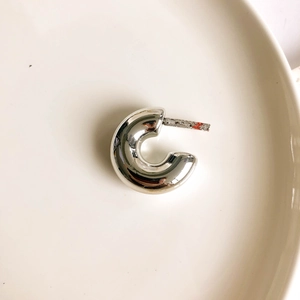 Macro shot of silver C-shaped hoop earring on a white ceramic plate with mirror finish