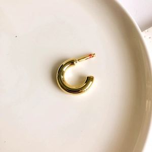Close-up of a polished gold-plated C-shaped hoop earring on a minimalist ceramic plate