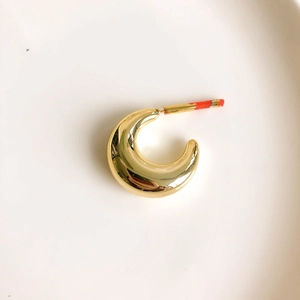 Detailed macro view of a chunky gold-plated croissant hoop earring with mirror finish