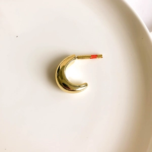 Top-down view of a chunky gold crescent earring on a clean white ceramic tray