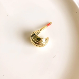 Close-up of golden C-shaped hoop earring with textured waves on a ceramic tray