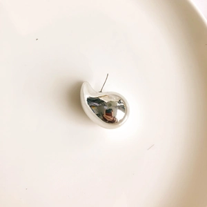 Close-up of a silver waterdrop earring with a mirror-polished finish on a white tray