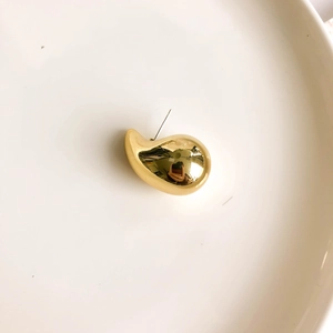 Macro view of gold teardrop stud earrings with a high-polished mirror finish in a tray