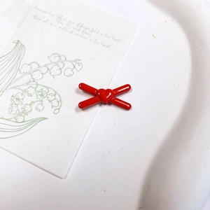 Gros plan de perles en forme de cœur rouge et accessoires DIY sur un plateau blanc