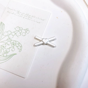 Détail de la pince à cheveux X en argent mat avec cœur sur un plateau blanc