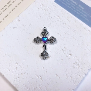 Macro shot of silver cross pendant with heart-shaped gem and rose flower carvings