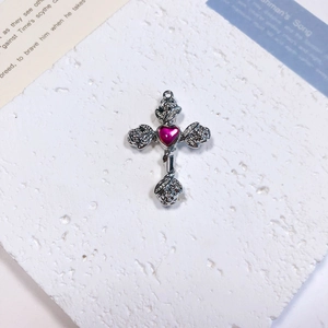 Macro detail of a silver cross pendant with rose relief and a red heart gemstone center