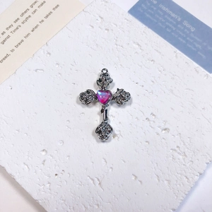 Macro detail of silver cross pendant with pink heart gemstone and rose floral relief