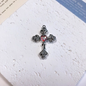 Detailed macro view of a silver alloy cross pendant with rose reliefs and a red heart gem